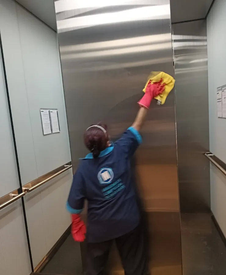 Colaboradora limpiando interior de elevador de acero inoxidable
