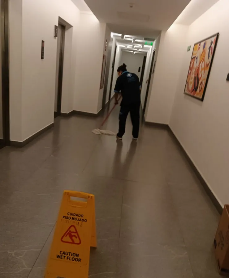 Colaboradora trapeando pasillo con señalamiento de piso mojado
